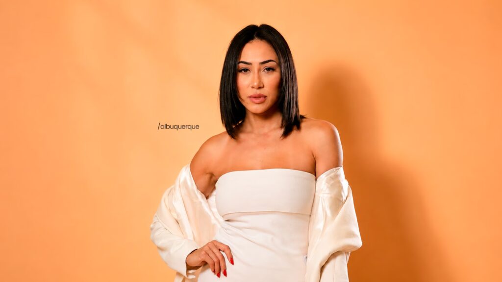Amanda Albuquerque está usando um vestido branco. Ela está com a mão direita na cintura.