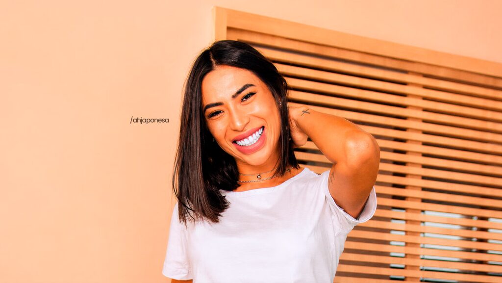 Beatriz Miuky com a mão na nuca. Ela está olhando para a frente e sorrindo.