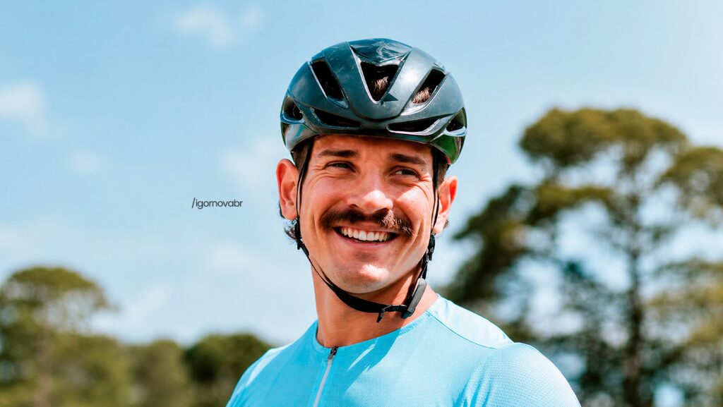 Igor Nova sorrindo. Ele está usando um capacete de ciclista.
