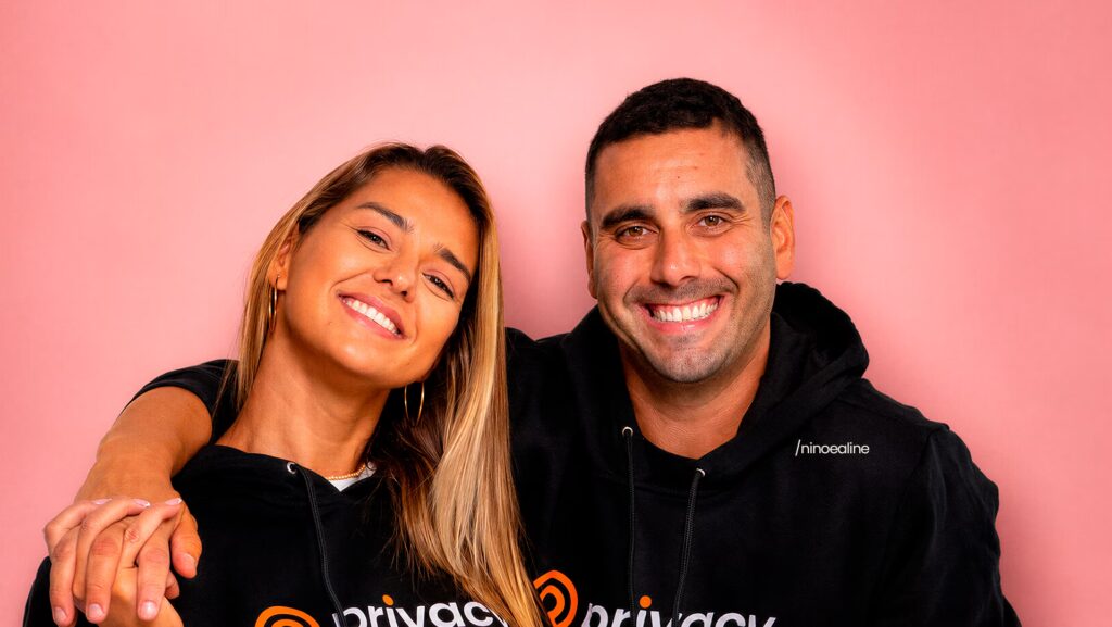 Nino e Aline estão se abraçando enquanto olhando com semblante feliz para frente.