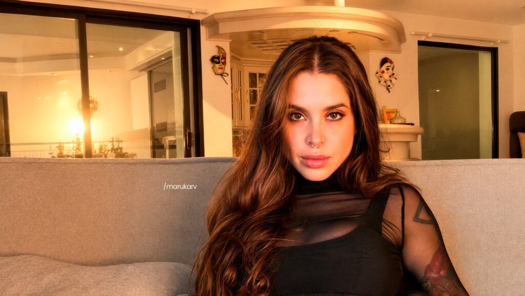 Maru olhando fixamente para a foto. Ela está sentada em um sofá bege.