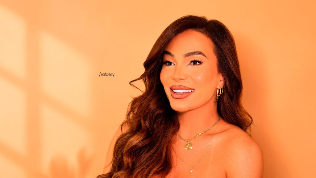 Rafaelly Pontes utilizando brincos e colares dourados. Ela está sorrindo e olhando para o horizonte.