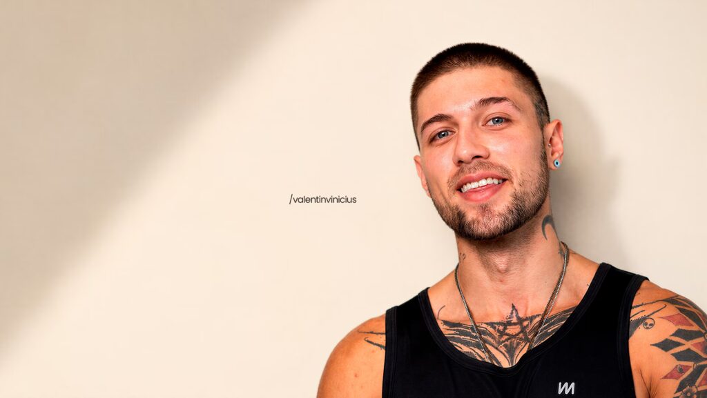 Vinicius Valentin sorrindo para a foto. Ele está usando um colar e uma regata preta