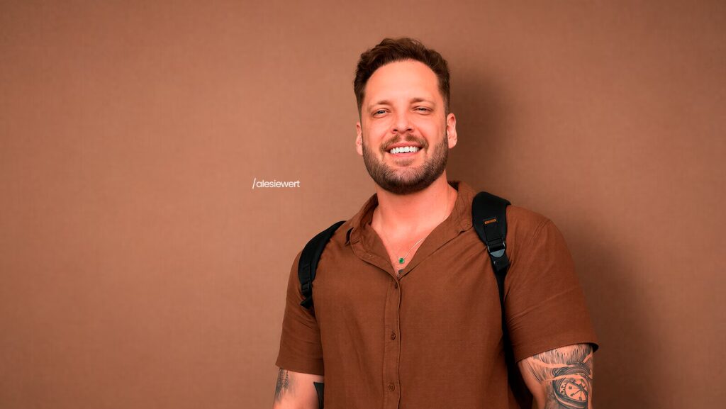 Ale Siewert sorrindo. Ele está com uma camisa marrom.