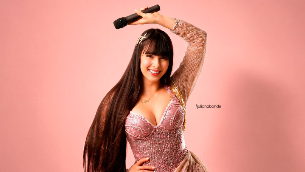 Juliana Bonde segurando um microfone . Ela está usando um vestido rosa.
