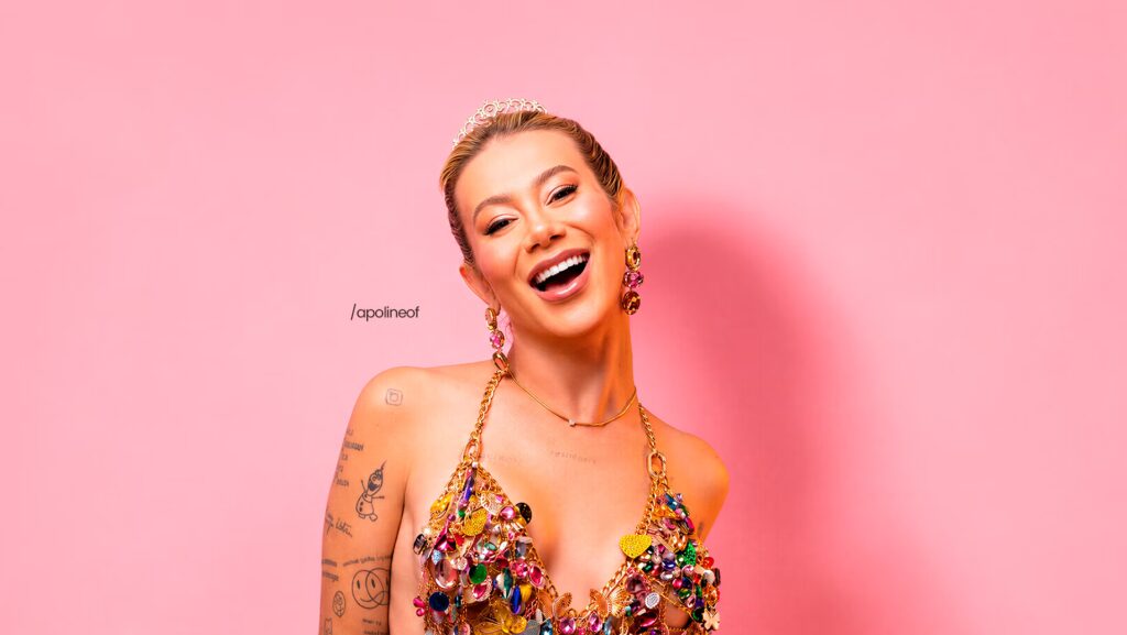 Apoline sorrindo para a foto. Ao fundo, uma parede rosa.