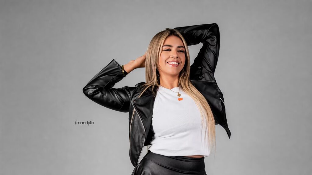 Mandy Lia está sorrindo para a foto com os dois braços levantados e as mãos tocando a parte de trás da cabeça.