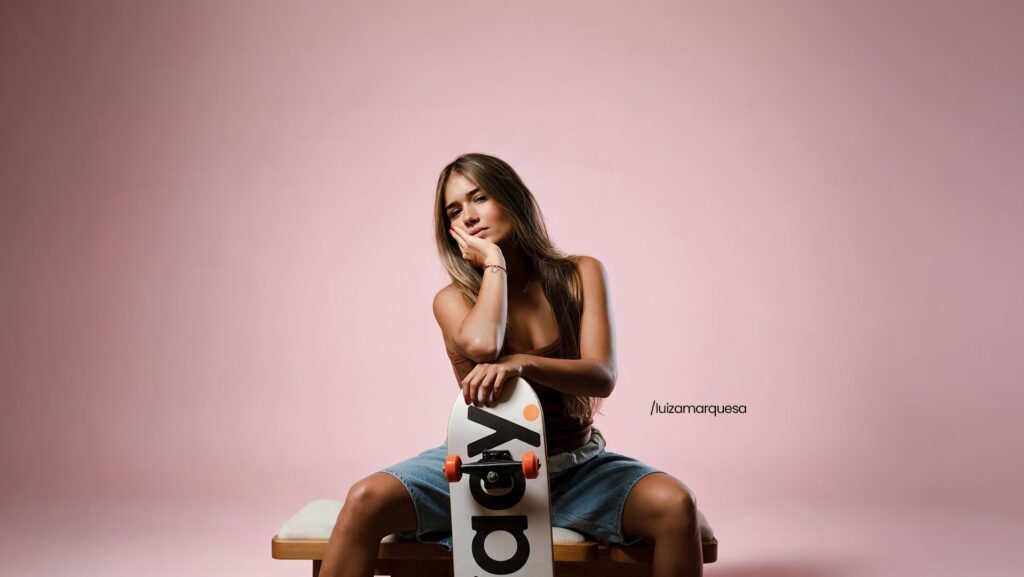 Luiza Marquesa sentada com a mão apoiada em seu rosto e segurando um skate.