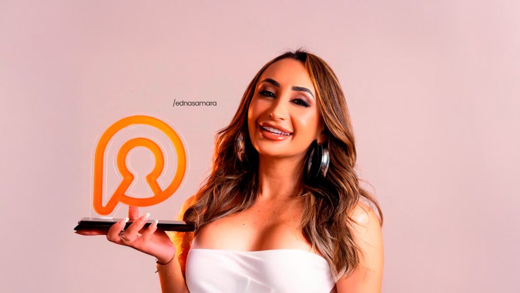 Edna Samara está sorrindo para foto. Ela segura com sua mão direita o troféu que ganhou da Privacy.
