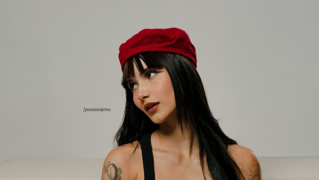 Paola Beatriz está utilizando uma boina vermelha. Enquanto olha para o lado em uma pose para a foto.