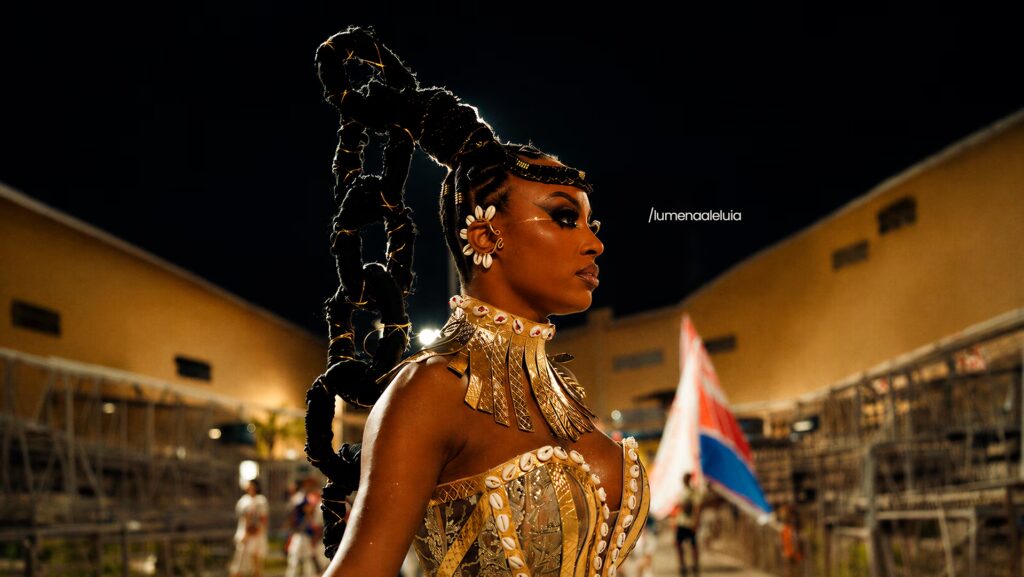 Lumena de perfil. Está vestindo uma roupa linda de carnaval.