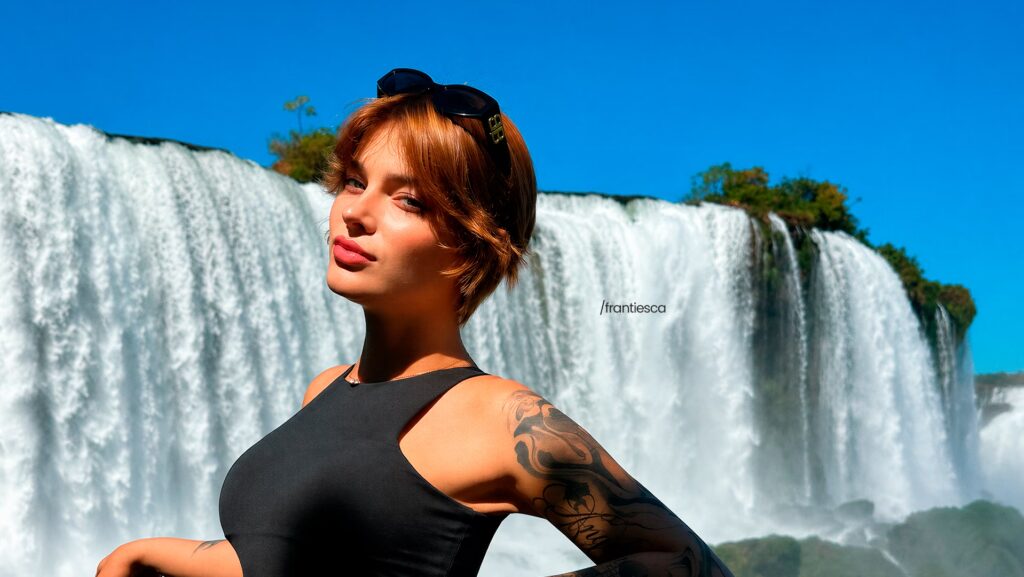 Frantiesca de perfil e olhando para frente. Ao fundo, uma cachoeira.