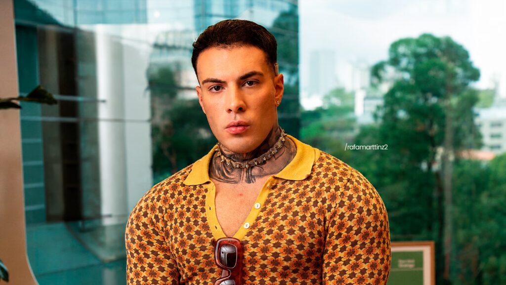 O Creator Rafa Martinz sentado olhando sério para a foto. Ele está utilizando uma camisa predominante amarela com algumas formas geométricas.