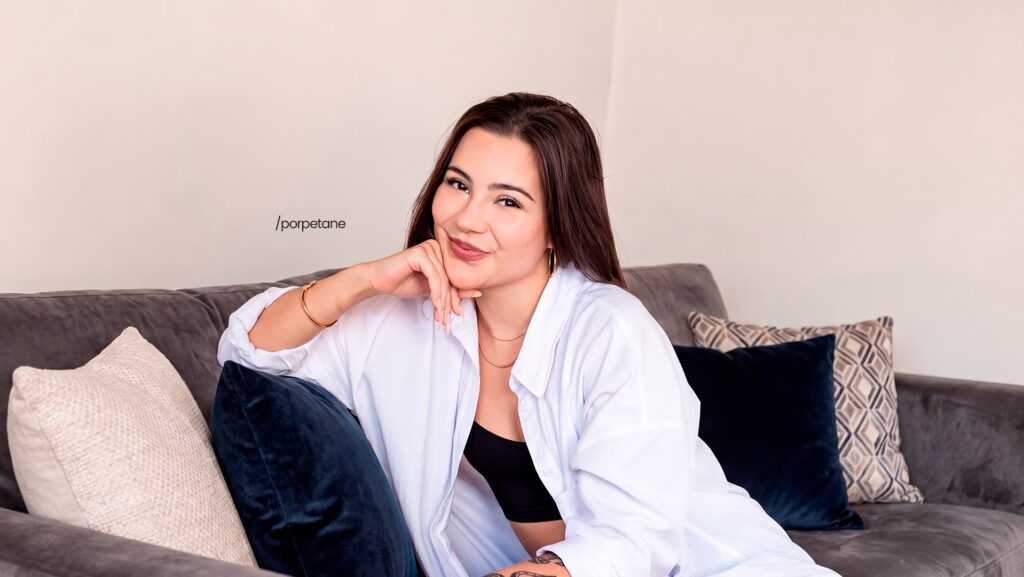 imagem da Influencer Porpetane sorrindo. Ela está sentada no sofá com a mão no queixo.