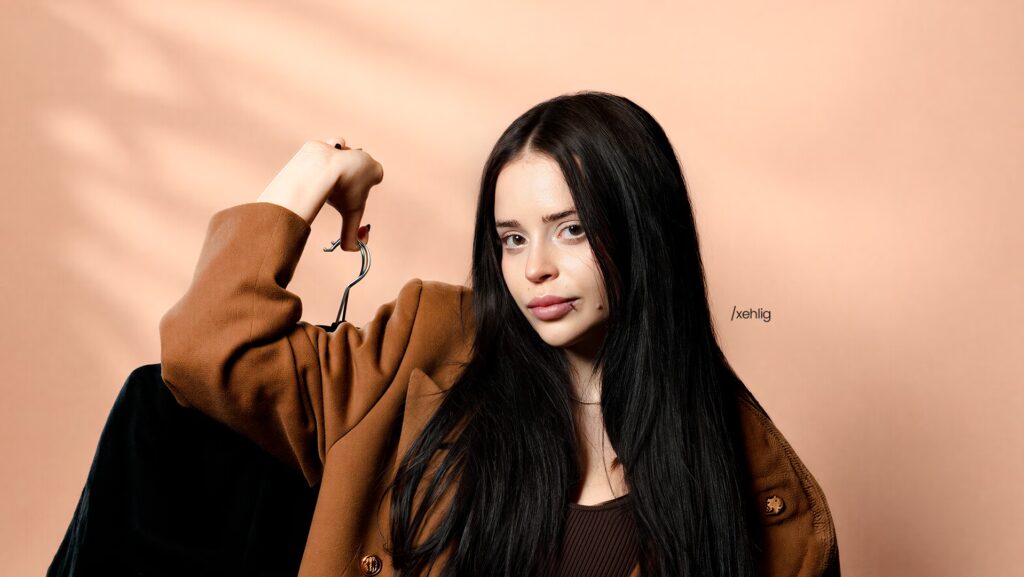 imagem da influiencer Xehli G. Ela está séria e segurando um cabide enquanto faz uma pose para a foto.