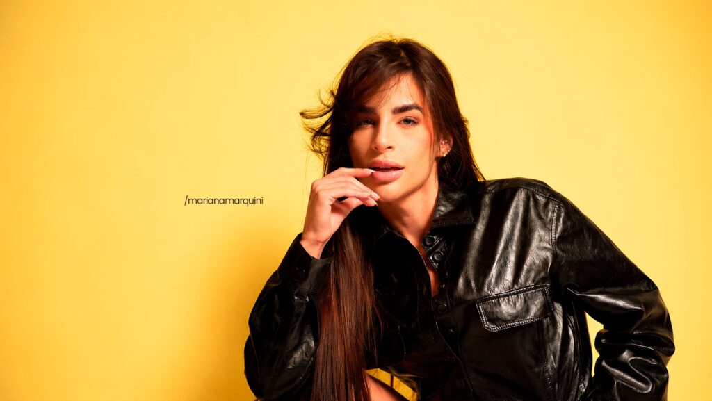 Mari Marquini sentada. Ela está com uma das mãos no queixo.