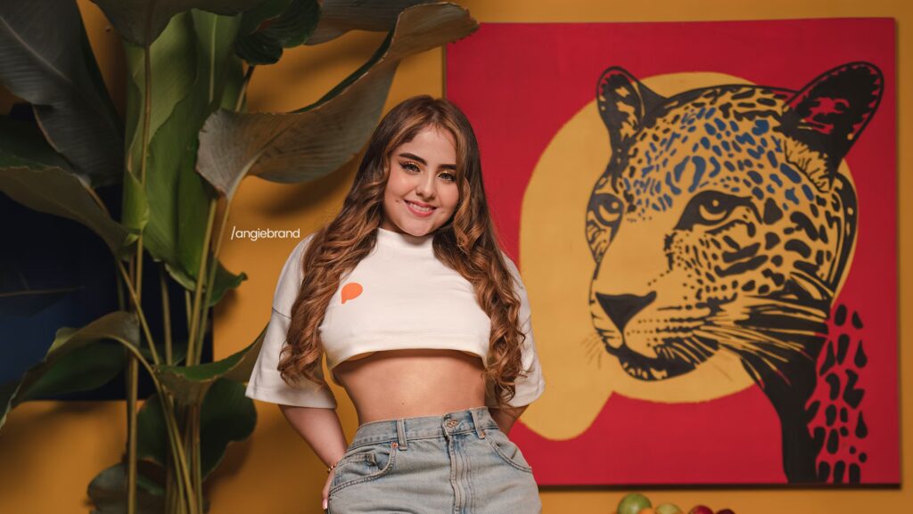 Creator Angie Brand está sorrindo e olhando para frente. As mão delas estão para trás.
